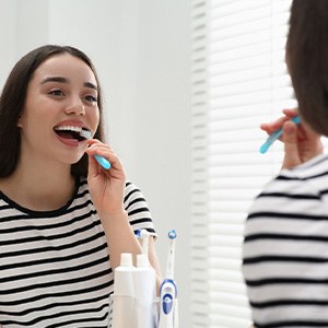 Woman smiling while brushing her teeth in bathroom