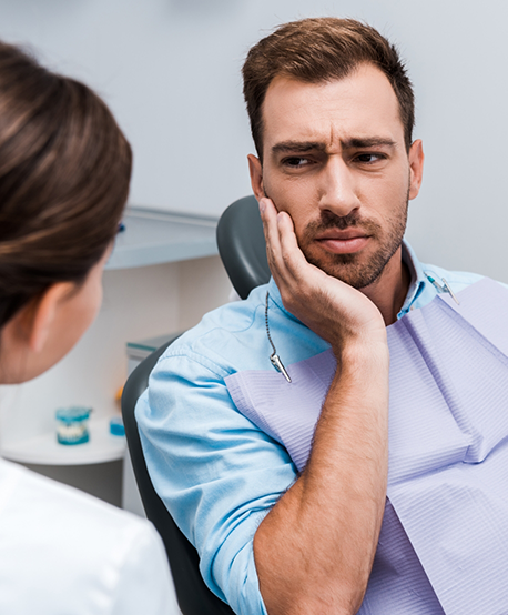 Man holding his cheek in pain while listening to his dentist