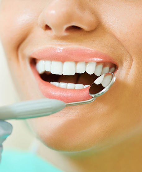Close up of a dental mirror right outside of a smiling mouth