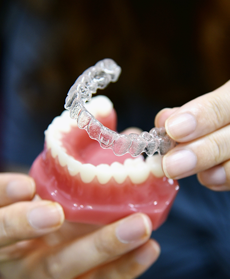 Dentist placing an Invisalign clear aligner over a model of a row of teeth