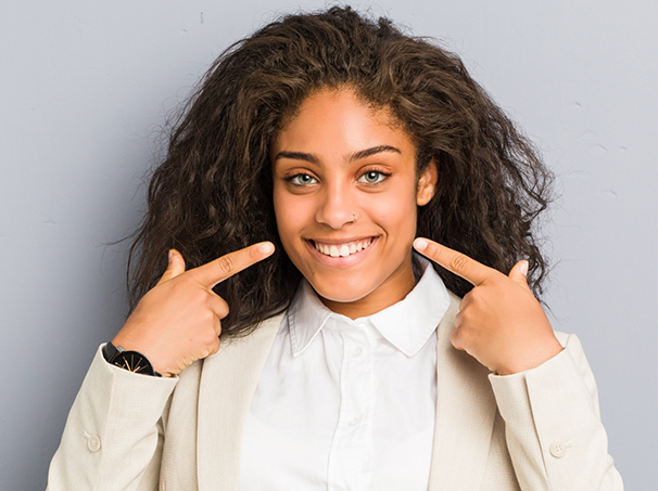 Woman with flawless teeth pointing to her smile after cosmetic dentistry in Westbury