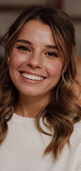 Young woman with curly brown hair smiling after dental services in Westbury