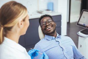 man sitting in dental chair speaking to dentist